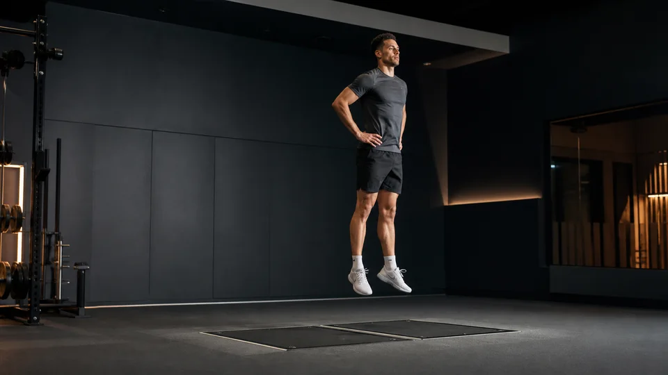 Atleta realizando un salto con contramovimiento, con las manos en las caderas, sobre dos plataformas de fuerza en un laboratorio de rendimiento.
